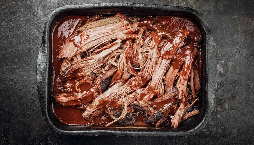 Saftiges pulled pork auf dem grill, in einer dunklen Schale mit BBQ-Sauce übergossen.