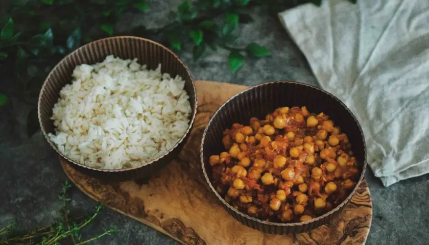 Schüssel mit Reis und eine Schüssel mit würzigem Chana Masala, serviert auf einem Holzbrett.