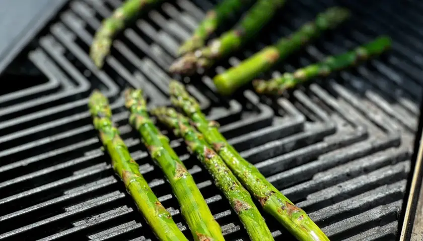Frischer Spargel grillen auf einem Gasgrill. Die grünen Stangen werden von der Hitze leicht gebräunt und verströmen ein köstliches Aroma.