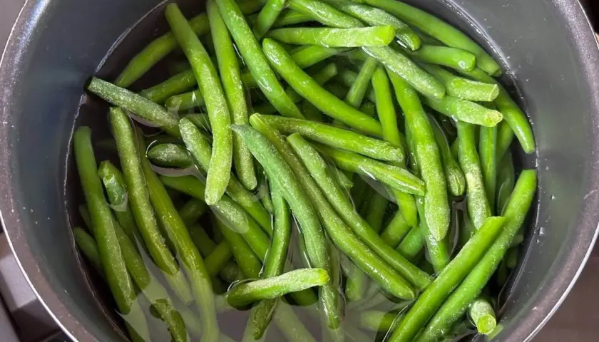 Grüne Bohnen kochen in einem Topf mit Wasser. Sie sind frisch und leuchtend grün, bereit für eine gesunde Mahlzeit.