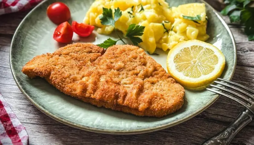 Knuspriges Putenschnitzel, mariniert und perfekt gegrillt, serviert mit Kartoffelsalat, Tomaten und Zitrone. Ein Genuss!