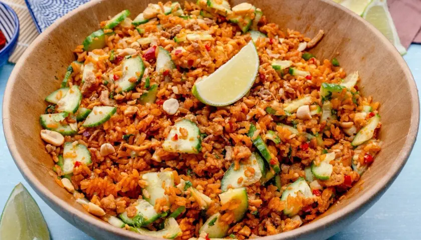Ein Schüssel mit knusprigem Reis Salat, garniert mit Gurkenscheiben, Erdnüssen und Limettenspalten.