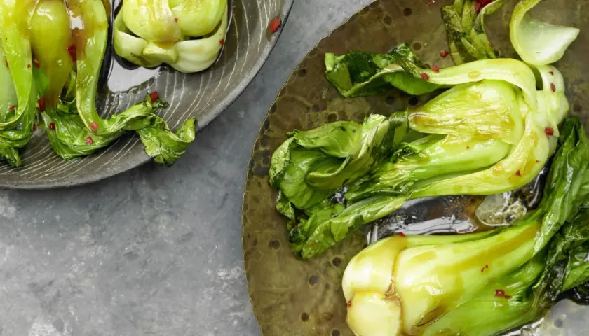Zwei Teller mit gedünstetem Pak Choi, glänzend von einer Sauce und bestreut mit roten Chiliflocken.