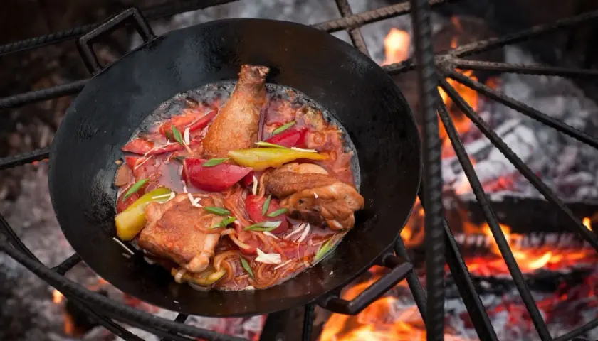 Hähnchen mit Gemüse in einer Pfanne über offenem Feuer. Tolle Camping Essen Ideen für ein herzhaftes Mahl.