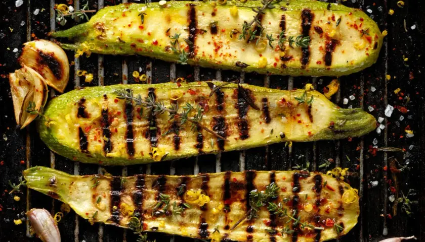 Perfekt gegrillte Zucchini-Scheiben mit Kräutern, Chili und Knoblauch auf dem Rost. Ein Genuss für jeden Grillmeister.