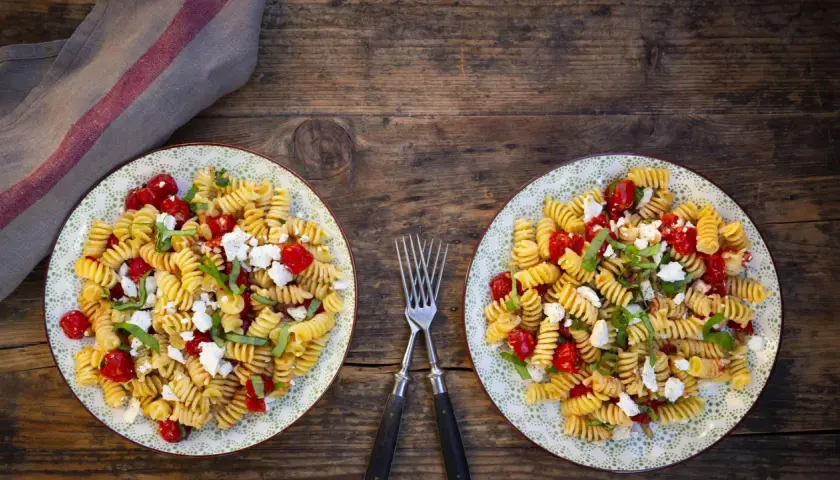 Zwei Teller mit leckeren schnellen Salaten ohne Mayo: Fusilli mit Kirschtomaten, Feta und Basilikum auf rustikalem Holztisch.