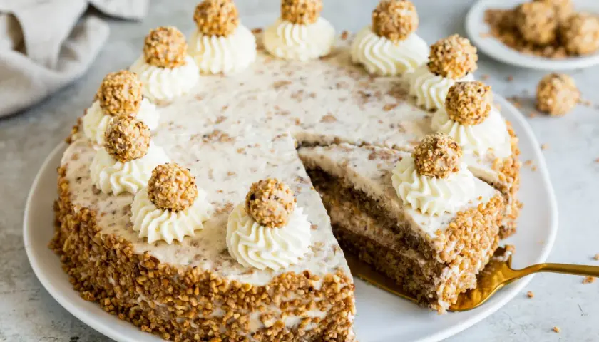 Eine köstliche Giotto Torte, verziert mit Sahnetuffs und Haselnusskugeln, umgeben von gehackten Nüssen.