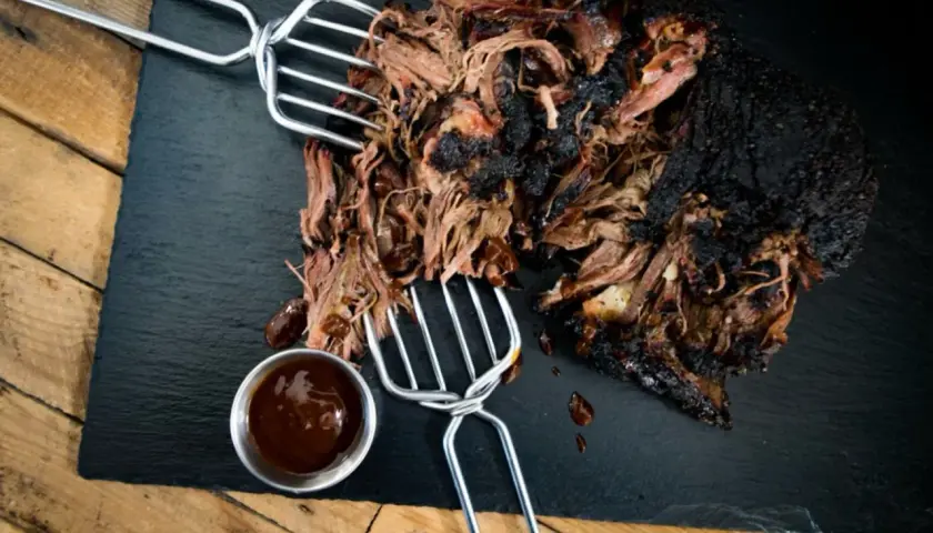 Zartes pulled beef mit dunkler Kruste, serviert mit BBQ-Sauce auf einem Schieferbrett.