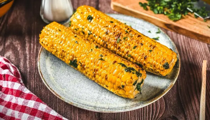Zwei goldgelbe Maiskolben, perfekt gegrillt und mit Kräutern bestreut, liegen auf einem Teller. Ein Genuss für alle Sinne!