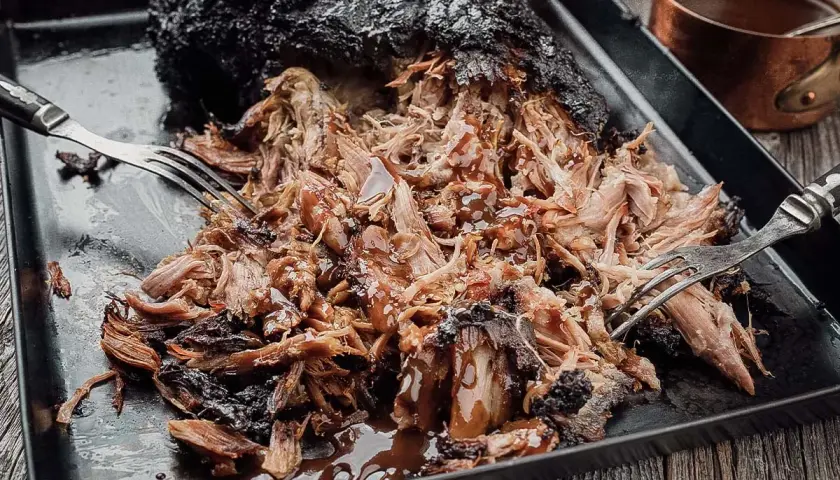 Saftiges Pulled Pork, frisch aus dem Smoker, mit einer dunklen Kruste und glänzender BBQ-Sauce. Zwei Gabeln zerreißen das Fleisch.