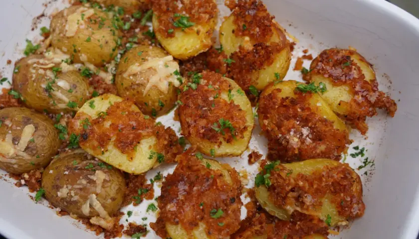 Knusprige parmesan kartoffeln mit Kräutern und grobem Salz bestreut, in einer weißen Auflaufform.