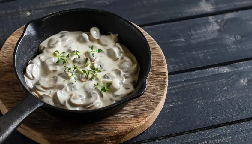 Cremige Champignon Rahmsauce in einer Gusseisenpfanne, garniert mit frischem Thymian.