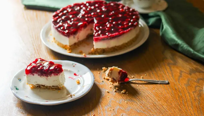 Ein köstlicher Kuchen ohne Backen mit Kirschtopping. Ein Stück auf einem Teller, ein Löffel mit einem Bissen daneben.
