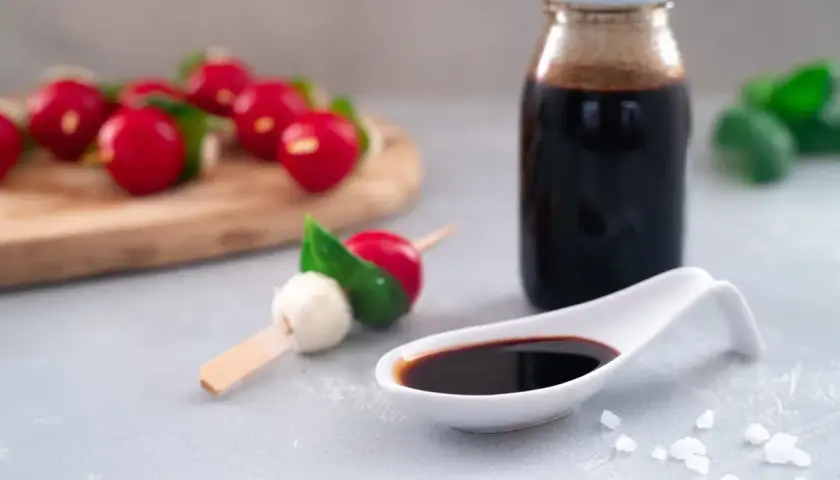 Ein Löffel mit dunkler balsamico creme, daneben eine Flasche und Radieschen-Mozzarella-Spieße.