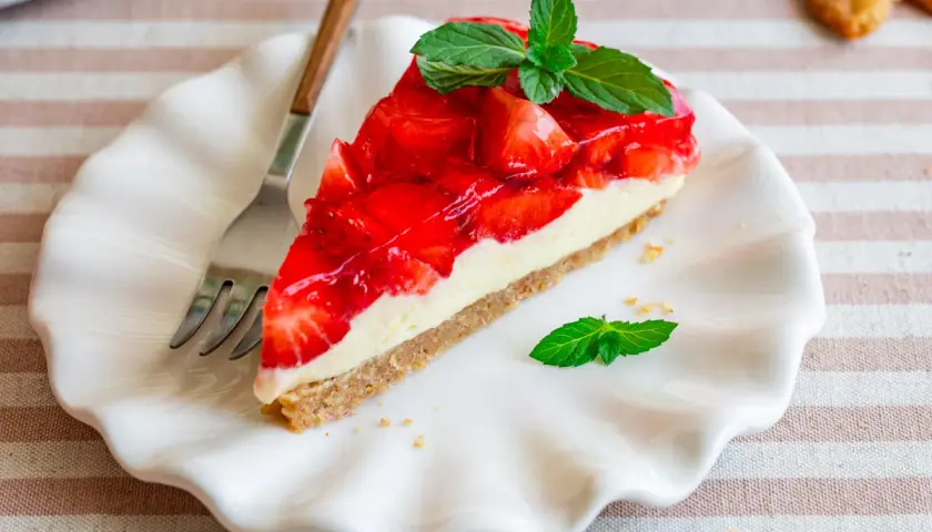 Ein Stück Erdbeerkuchen mit Keksboden, schnell und ohne Backen zubereitet. Frisch, fruchtig und mit Minze garniert.