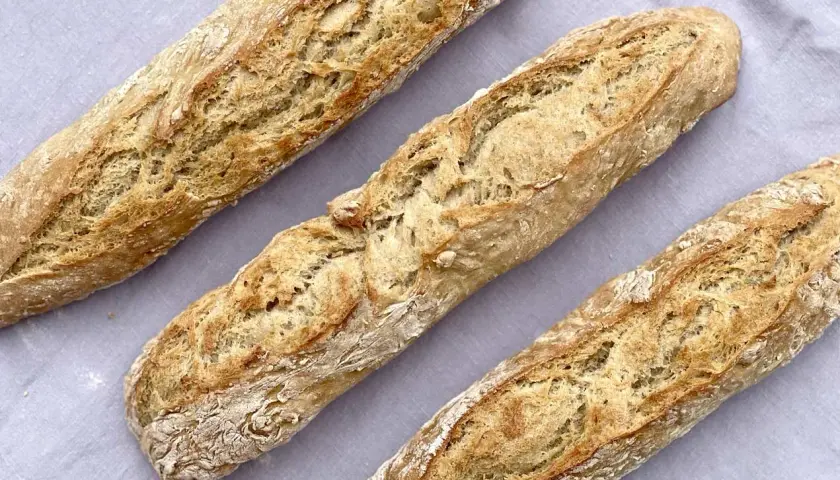 Drei frisch gebackene Baguettes mit knuspriger Kruste liegen auf einem grauen Tuch. Ein tolles Baguette Rezept zum Nachbacken!