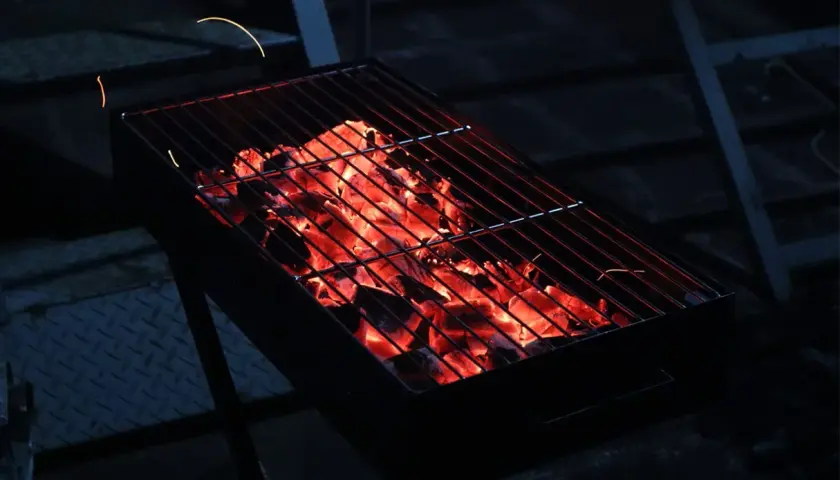 Glühende Kohlen unter dem Rost versprechen ein gemütliches Grillen mit Holzkohle. Funken tanzen in der Dunkelheit.