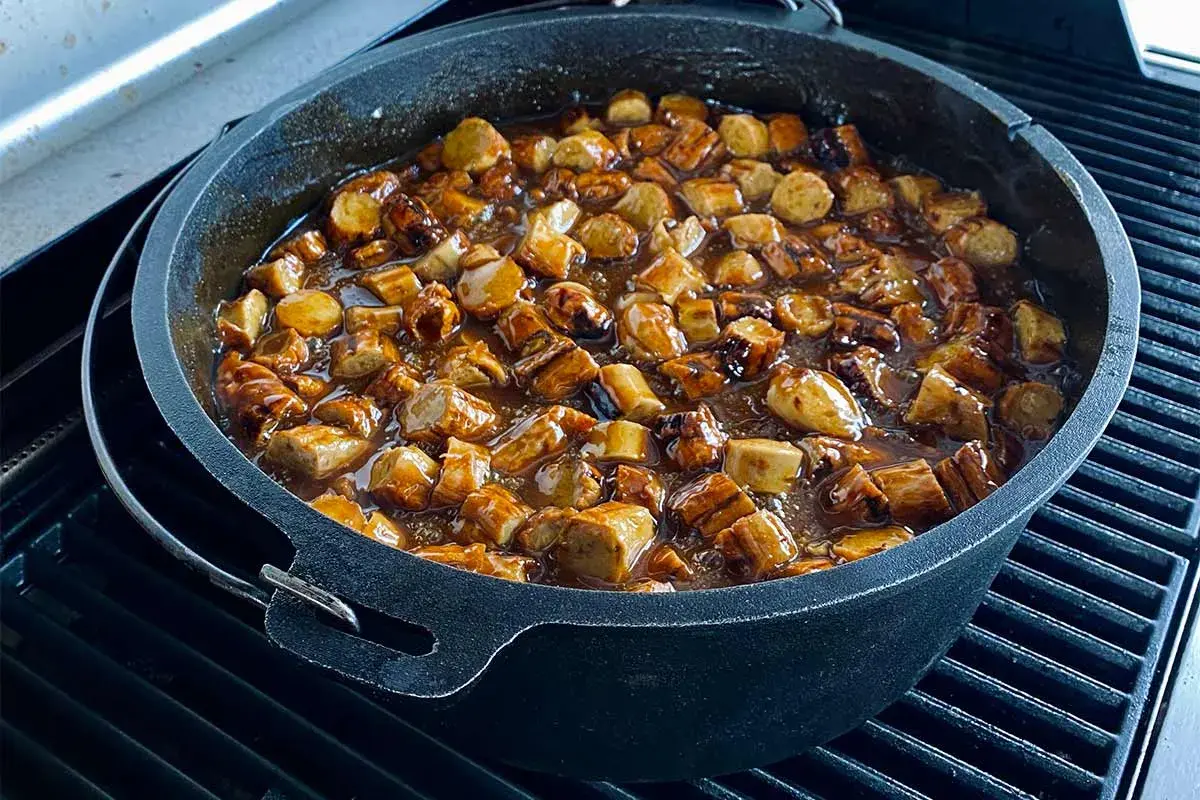 Leckere Currywurst-Stücke köcheln in einer würzigen Sauce in einem gusseisernen Dutch Oven auf dem Grill.
