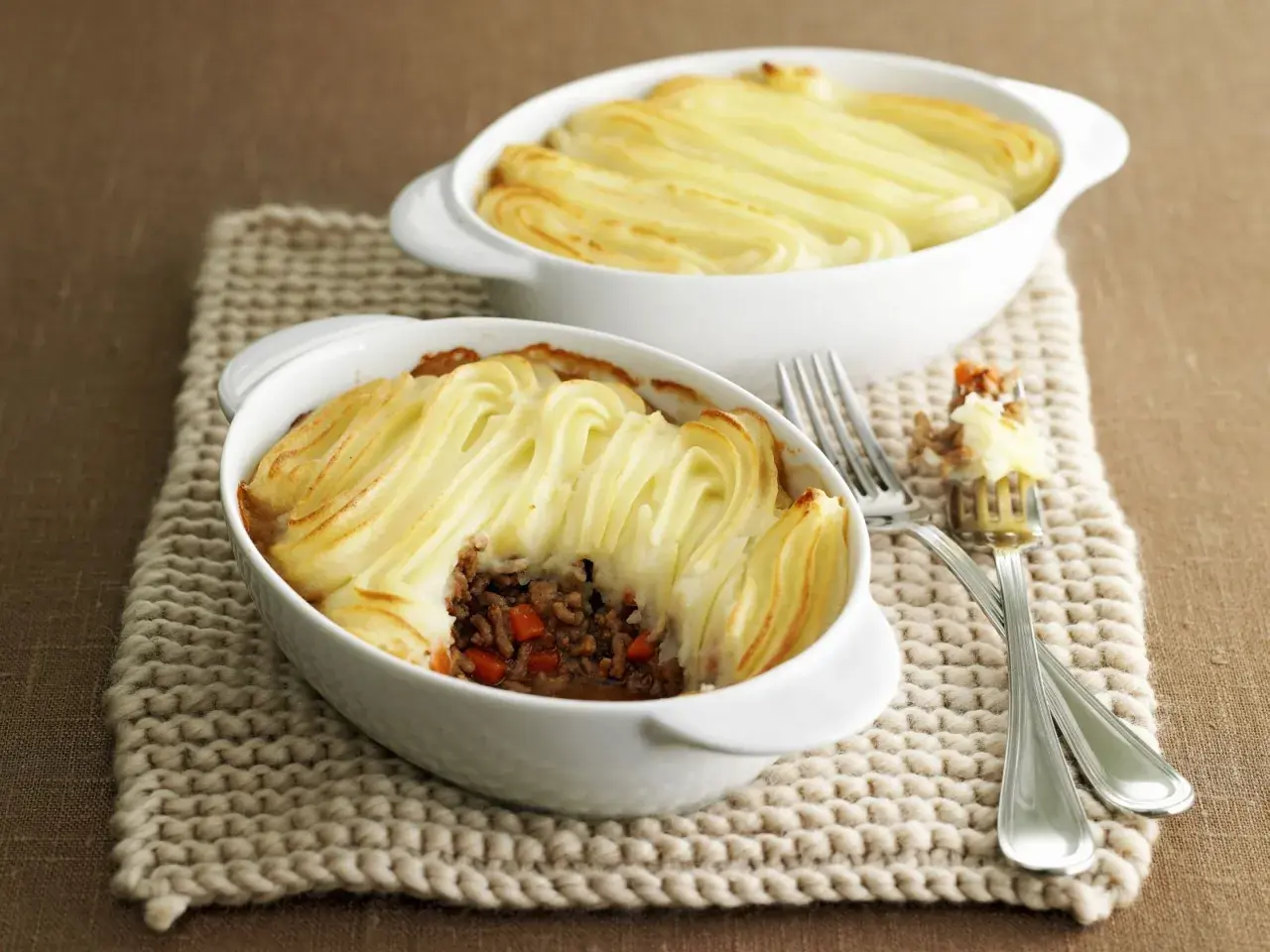 Zwei Auflaufformen mit goldbraunem Shepherd's Pie, bedeckt mit kunstvoll gespritztem Kartoffelpüree.
