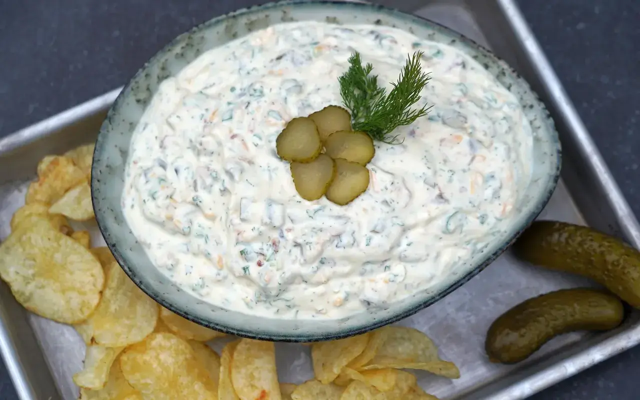Cremiger blue cheese dip mit Dill und Gurkenscheiben, serviert mit Kartoffelchips und Gewürzgurken.