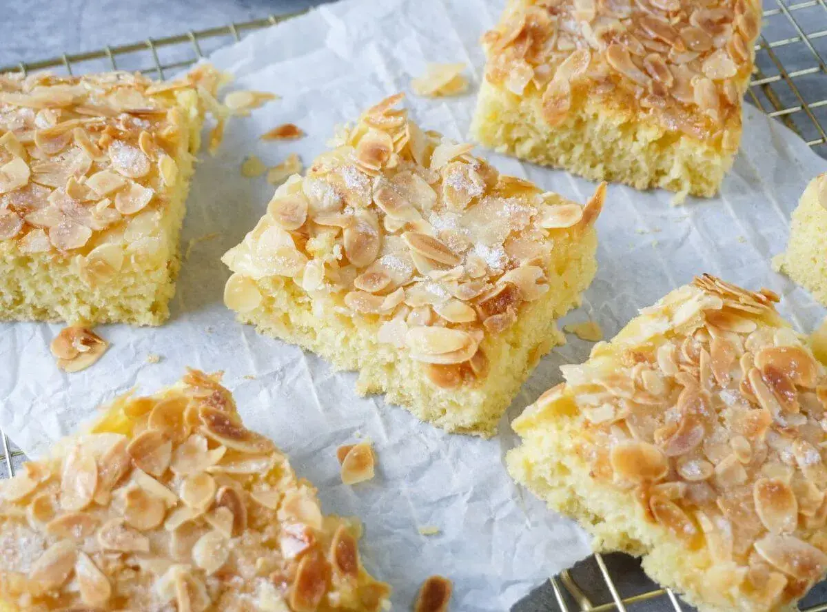 Saftiger Buttermilch Kuchen mit Mandelsplittern und Zucker bestreut, auf Backpapier und einem Gitter angerichtet.