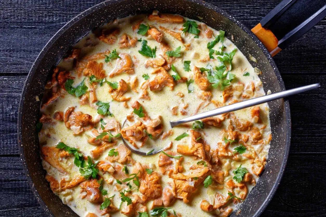 Pfifferlinge in cremiger Rahmsauce, garniert mit Petersilie, in einer Pfanne. Ein Löffel ragt aus der köstlichen Speise.