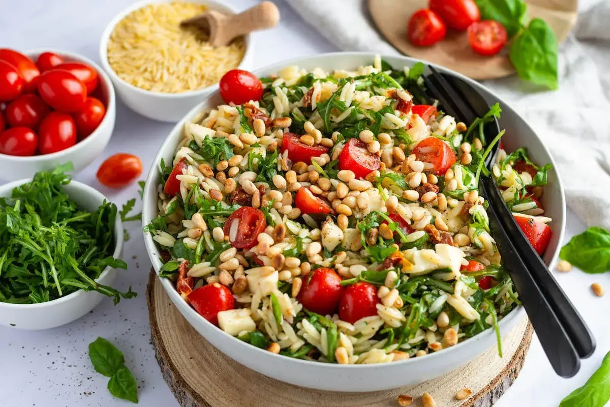 Frischer Nudelsalat mit Tomaten, Rucola und Pinienkernen – perfekt als Beilage zum Grillen.