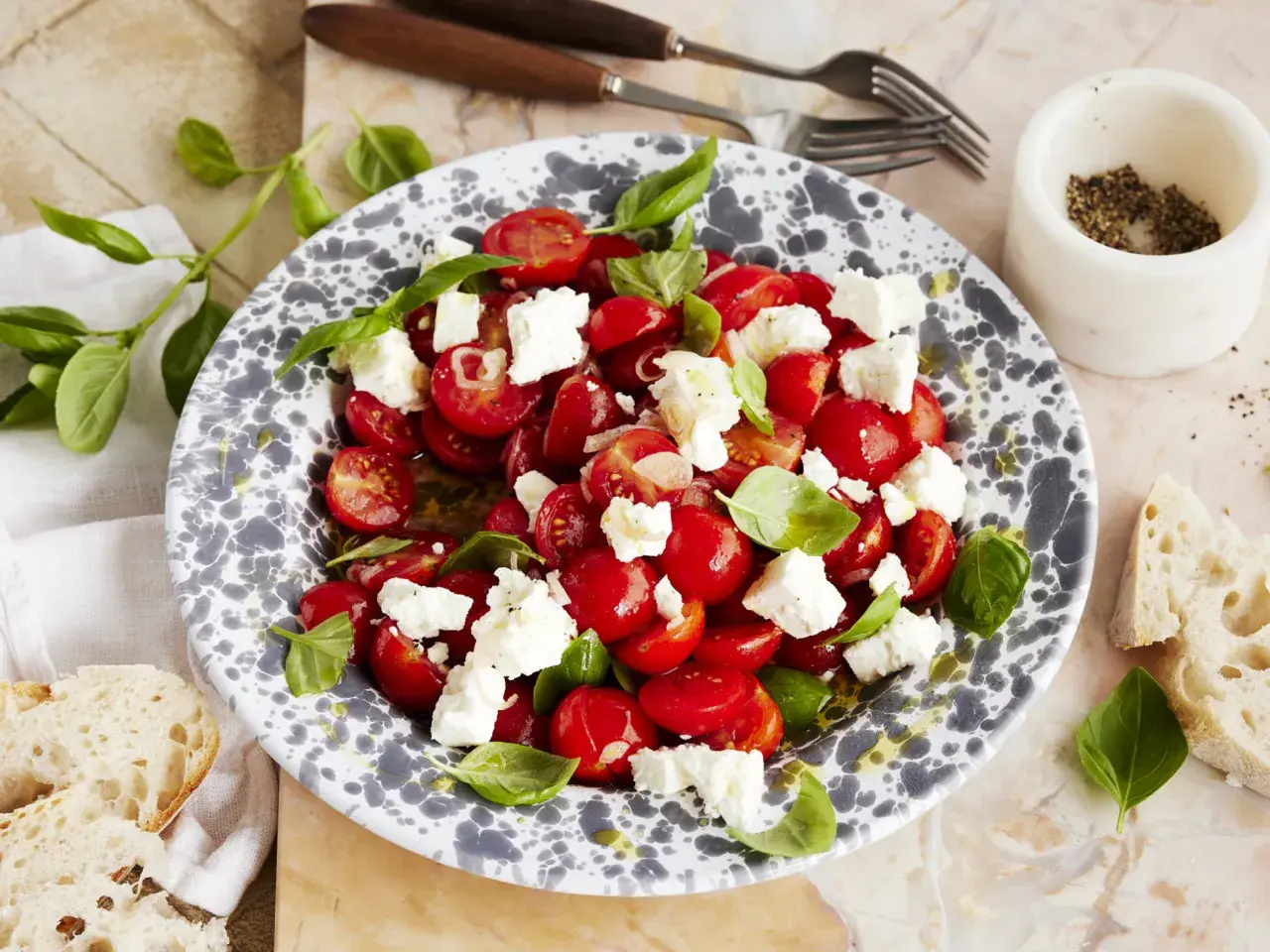Frischer tomatensalat mit feta, garniert mit Basilikum. Dazu gibt es knuspriges Brot.