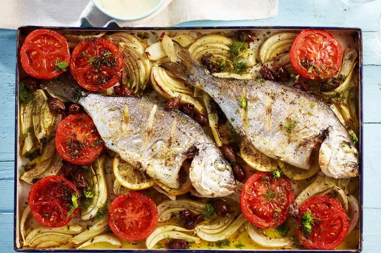 Zwei goldbrassen im backofen mit Tomaten, Fenchel und Oliven, appetitlich zubereitet.