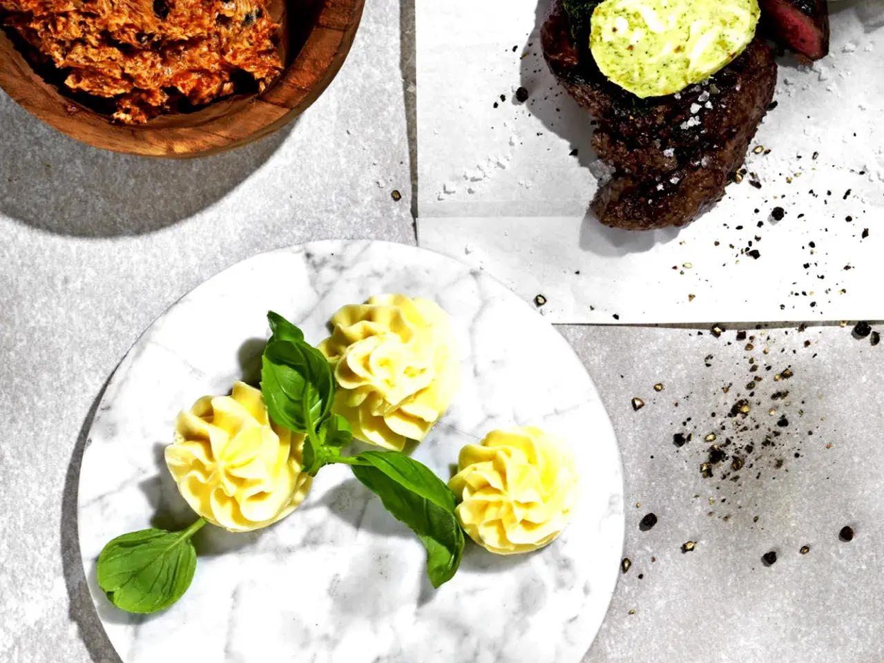 Knoblauchbutter rezept: Ein Steak mit Kräuterbutter, dazu Kartoffelröschen und eine Schüssel mit würziger Butter.