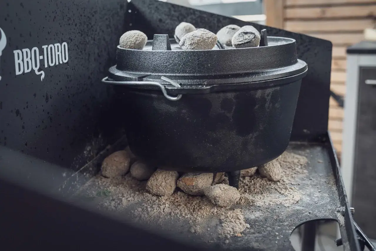 Ein Dutch Oven auf einem Gasgrill, bereit für ein köstliches Outdoor-Abenteuer. Glühende Kohlen sorgen für die perfekte Hitze.