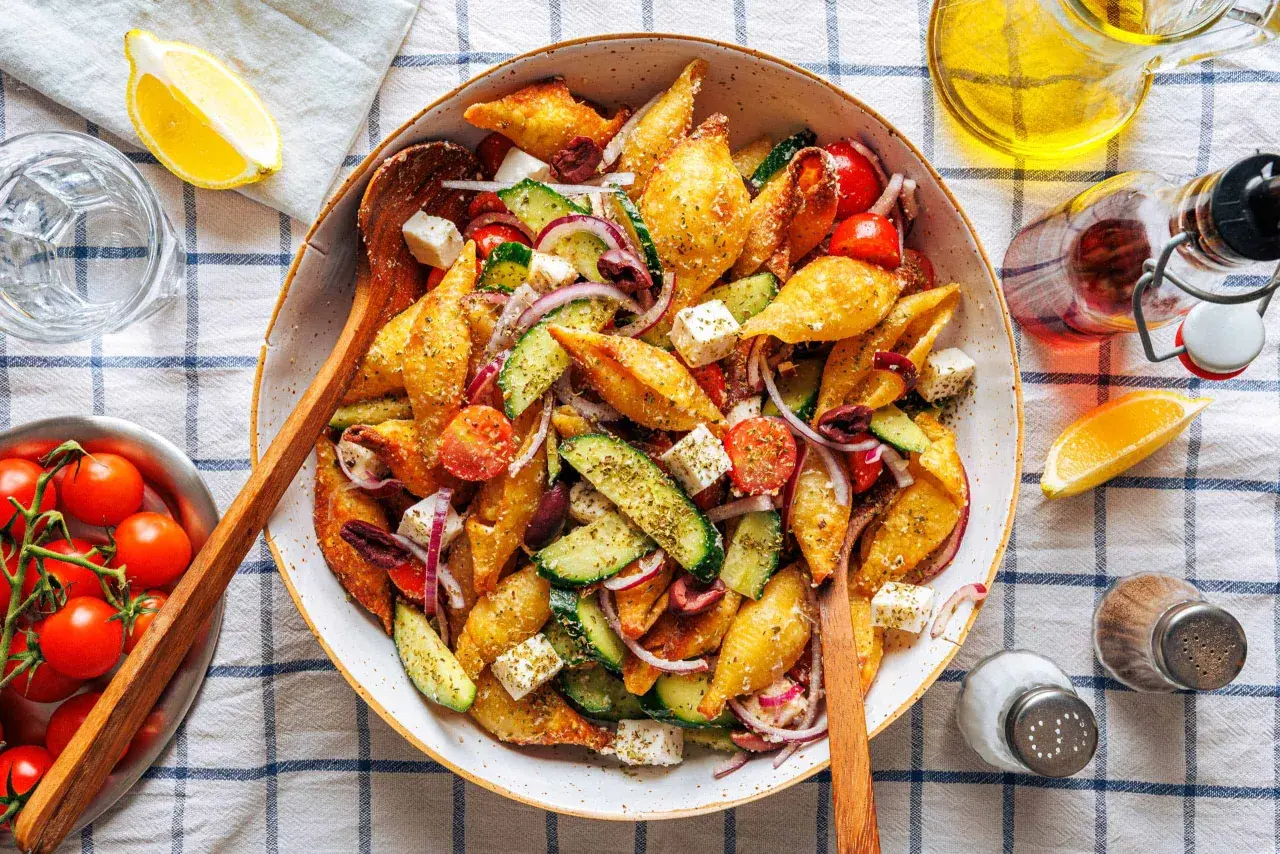 Ein bunter Nudelsalat mal anders: knusprige Muschelnudeln mit Gurke, Tomaten, Feta und roten Zwiebeln, garniert mit Kräutern.