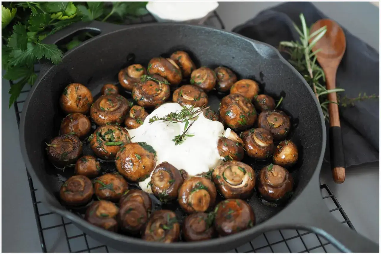 Gebratene Champignons mit Kräutern und cremiger Sauce in einer Gusseisenpfanne. Perfekt für leckere Champignons Rezepte.