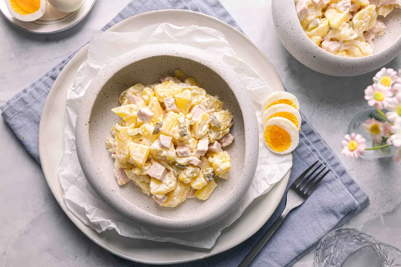 Ein cremiger Kartoffelsalat mit Mayonnaise, Schinken und Gewürzgurken, serviert mit gekochten Eiern. Ein klassisches Kartoffelsalat Rezept mit Mayonnaise.