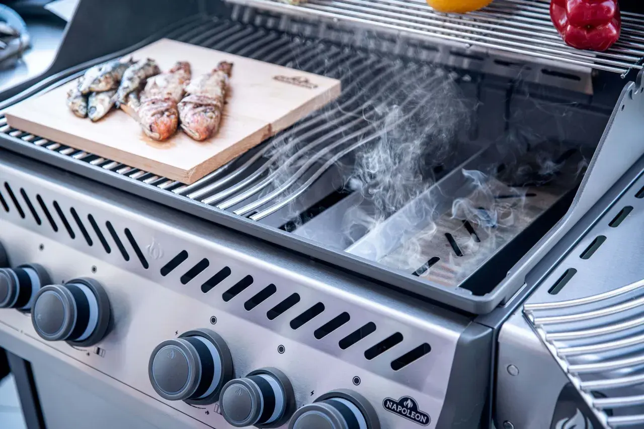 Fisch auf Holzbrett im Gasgrill, Rauch steigt auf. Leckeres Smoken im Gasgrill für ein besonderes Aroma.