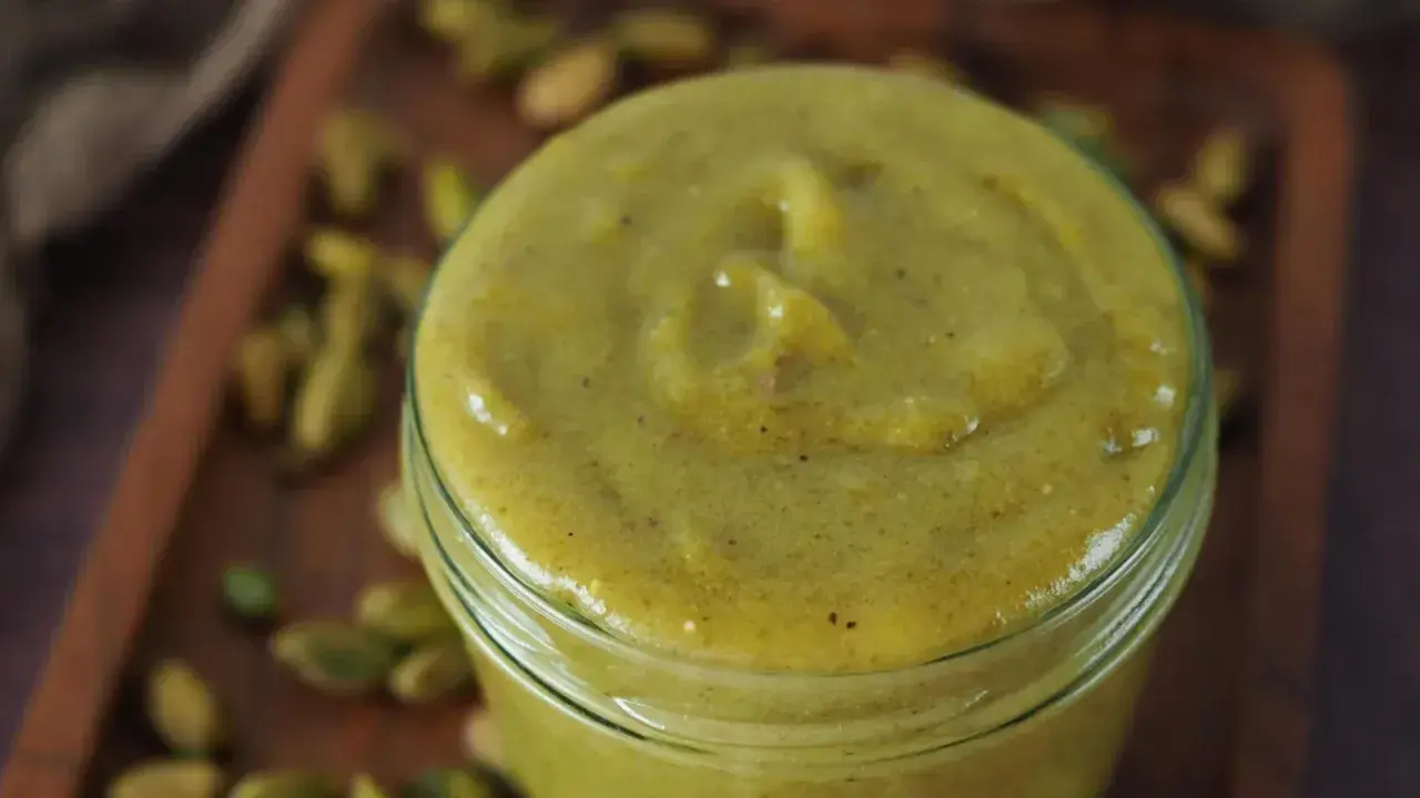 Selbstgemachte Pistaziencreme in einem Glas, umgeben von ganzen Pistazien. Perfekt zum Backen und Genießen.