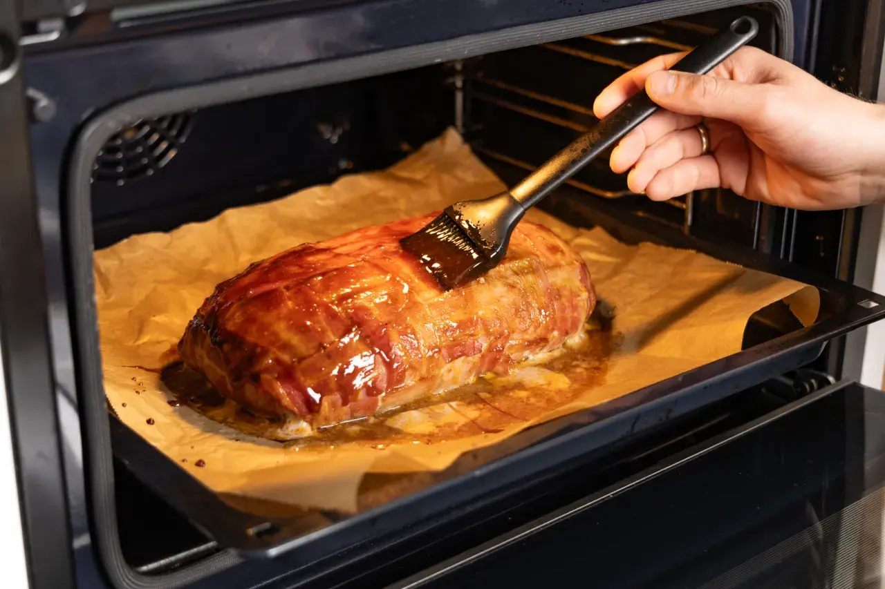 Ein Braten, umwickelt mit Bacon, wird im Backofen mit einer Glasur bestrichen. Die Bacon-Bomb-Zubereitung im Ofen ist fast fertig.