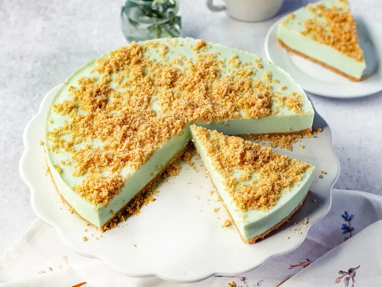 Eine cremige Philadelphia Torte Waldmeister mit knuspriger Streuselhaube, ein Stück ist bereits angeschnitten.