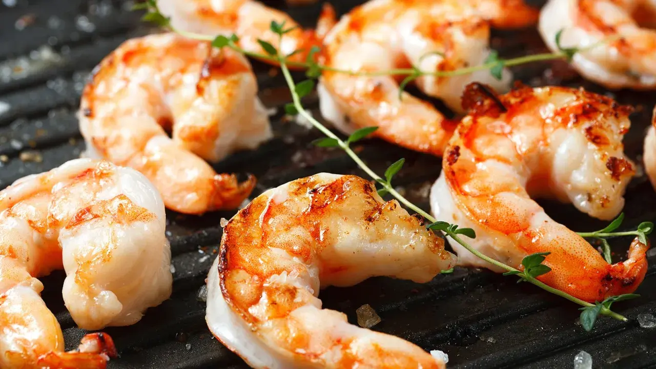Saftige black tiger Garnelen grillen auf einer heißen Grillplatte, garniert mit frischem Thymian.