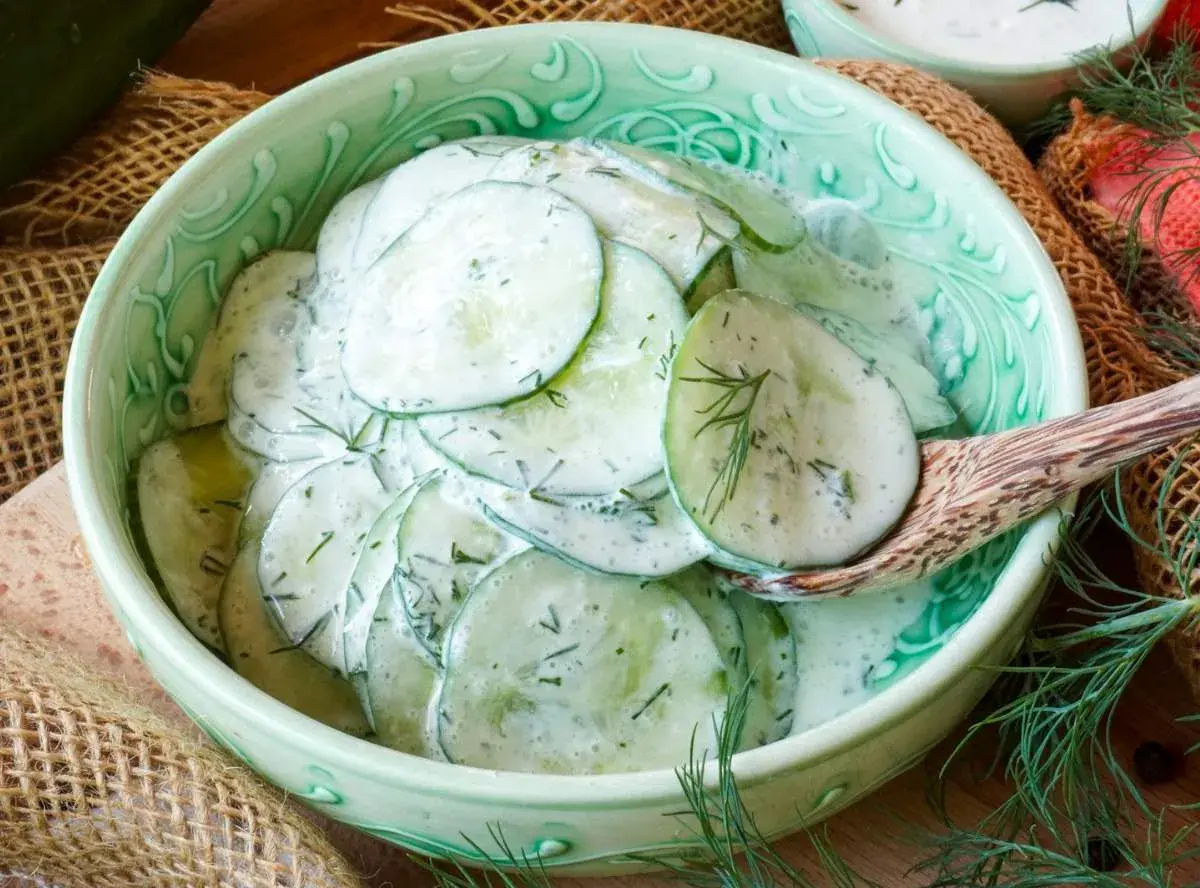 Frischer gurkensalat mit saurer sahne und Dill, serviert in einer grünen Schüssel mit einem Holzlöffel.