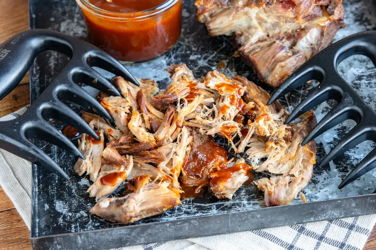 Zartes pulled pork sous vide, mit BBQ-Sauce beträufelt, bereit zum Zerreißen mit Fleischgabeln.