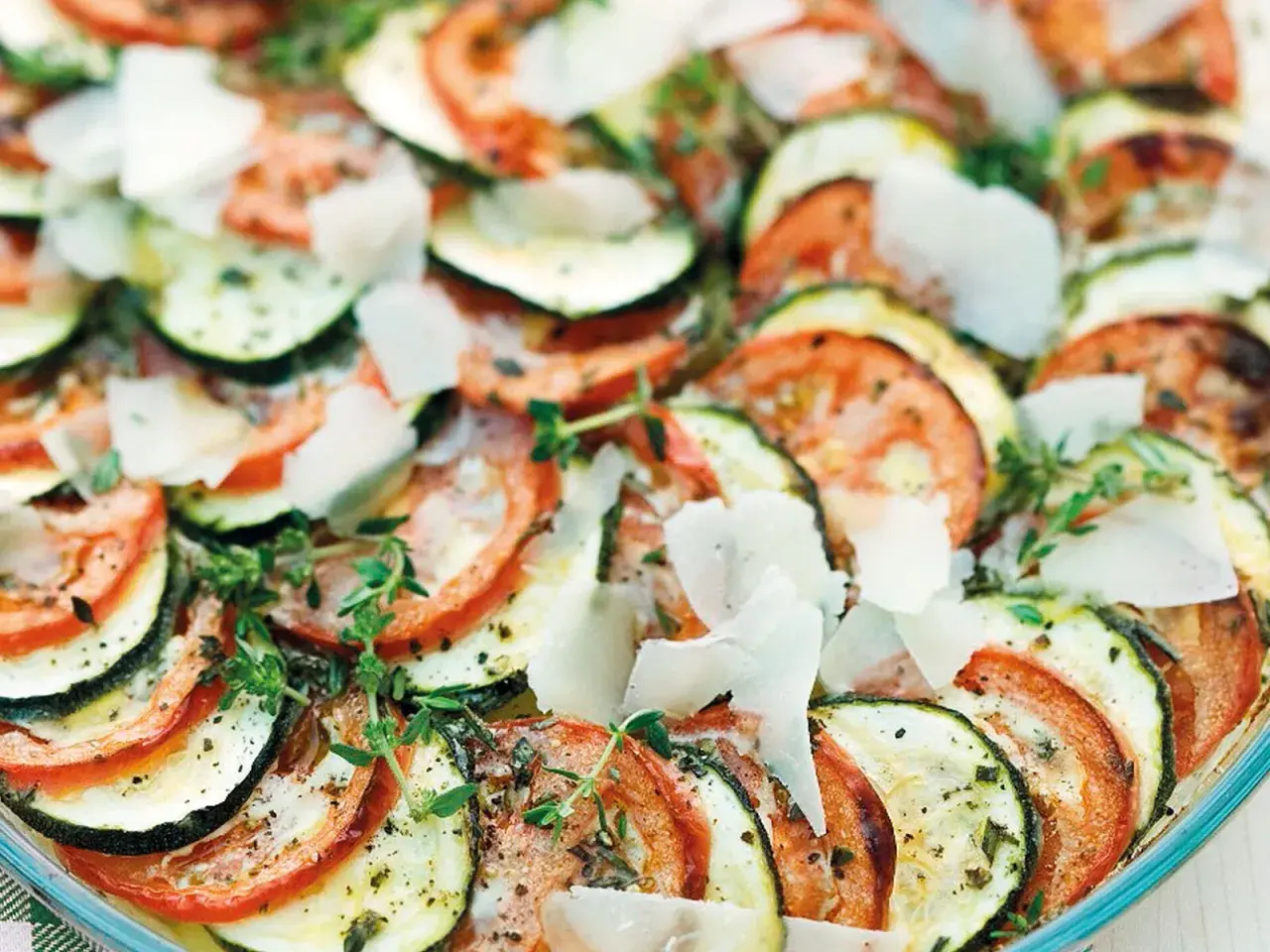 Schicht für Schicht ein Genuss: Ein köstlicher Tomaten Zucchini Auflauf, garniert mit Parmesan und frischen Kräutern.