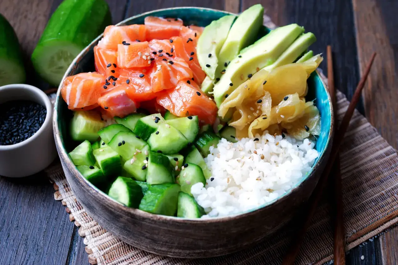 Eine bunte Sushi Bowl mit Lachs, Avocado, Gurke und Reis. Sesamkörner bestreuen die frischen Zutaten.