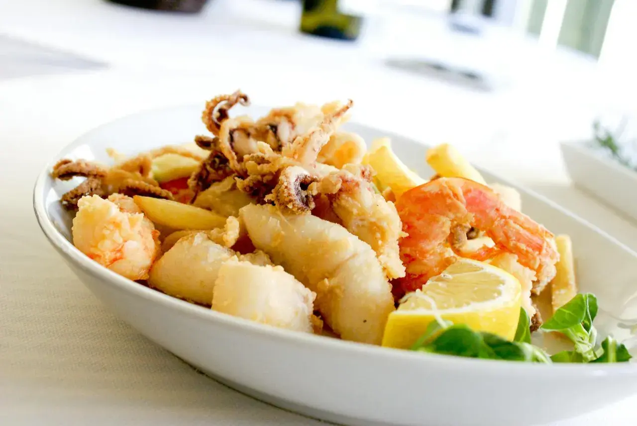 Knuspriges Fritto Misto mit Garnelen, Tintenfischringen und Fischstücken, garniert mit Zitrone und frischen Kräutern.