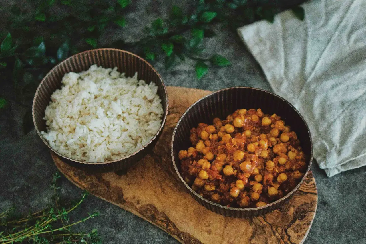 Schüssel mit Reis und eine Schüssel mit würzigem Chana Masala, serviert auf einem Holzbrett.
