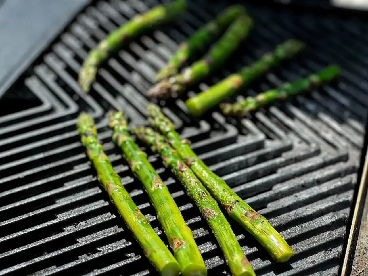 Frischer Spargel grillen auf einem Gasgrill. Die grünen Stangen werden von der Hitze leicht gebräunt und verströmen ein köstliches Aroma.