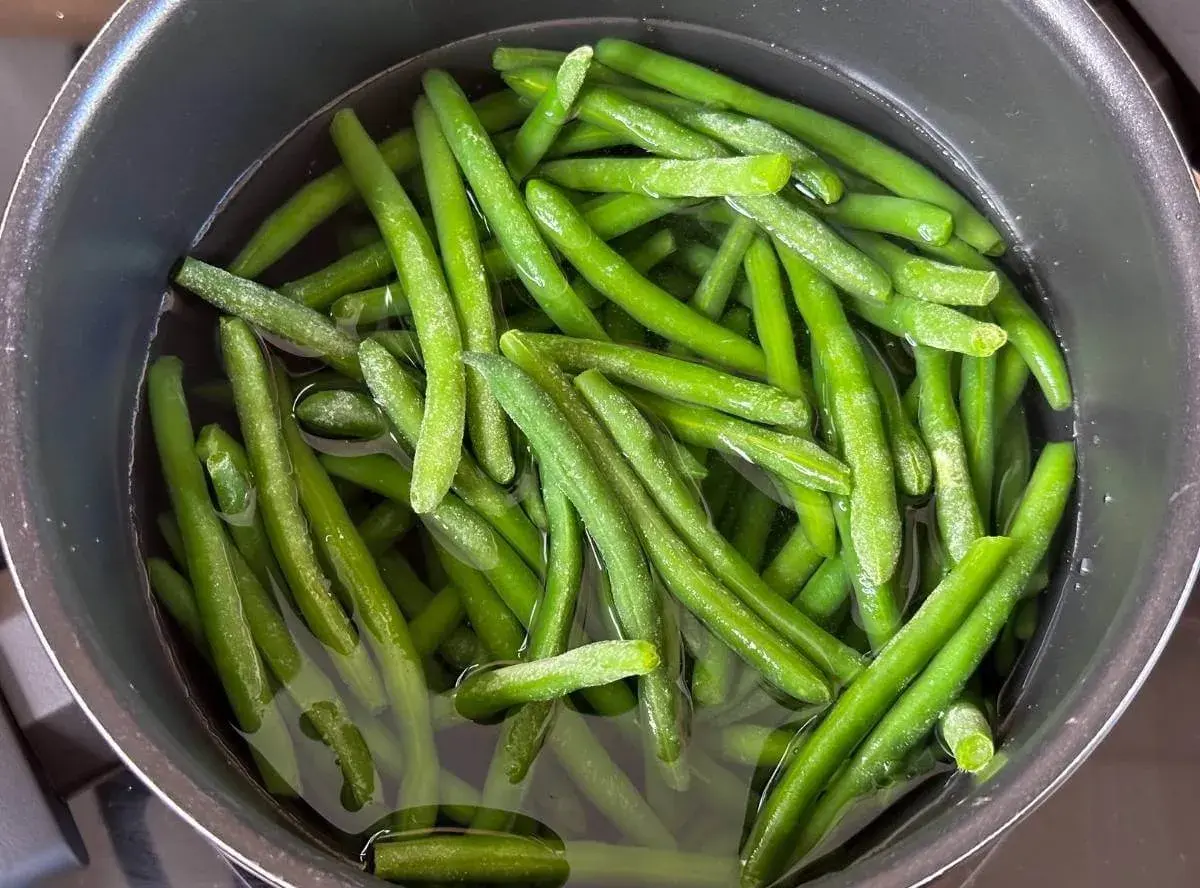 Grüne Bohnen kochen in einem Topf mit Wasser. Sie sind frisch und leuchtend grün, bereit für eine gesunde Mahlzeit.