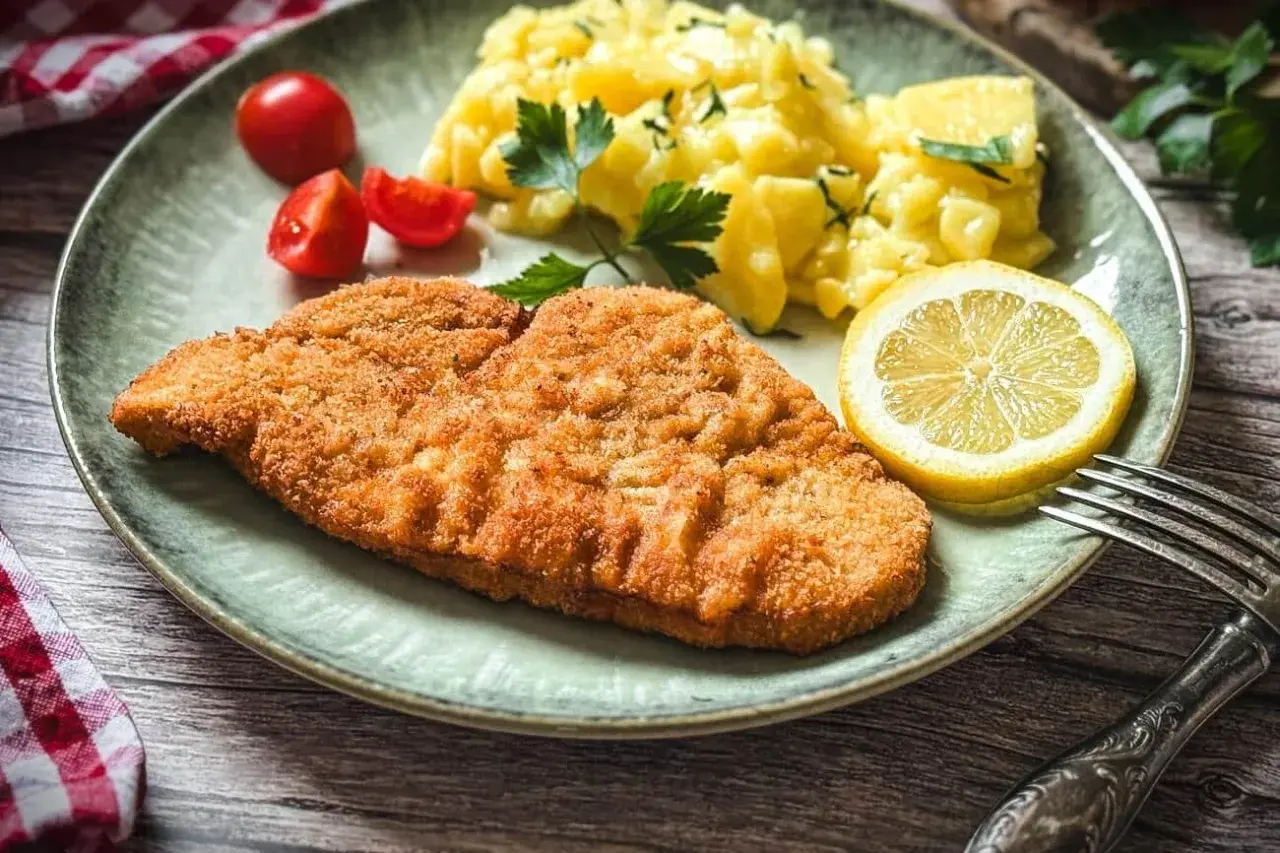 Knuspriges Putenschnitzel, mariniert und perfekt gegrillt, serviert mit Kartoffelsalat, Tomaten und Zitrone. Ein Genuss!
