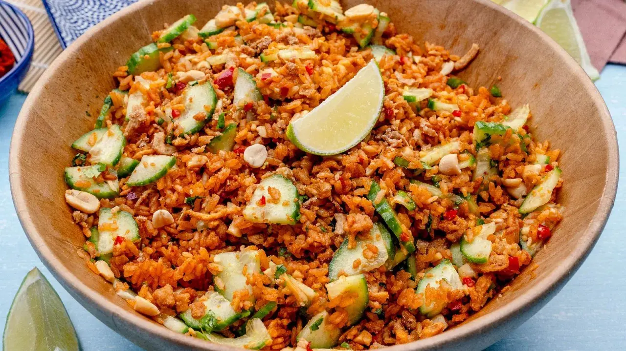 Ein Schüssel mit knusprigem Reis Salat, garniert mit Gurkenscheiben, Erdnüssen und Limettenspalten.