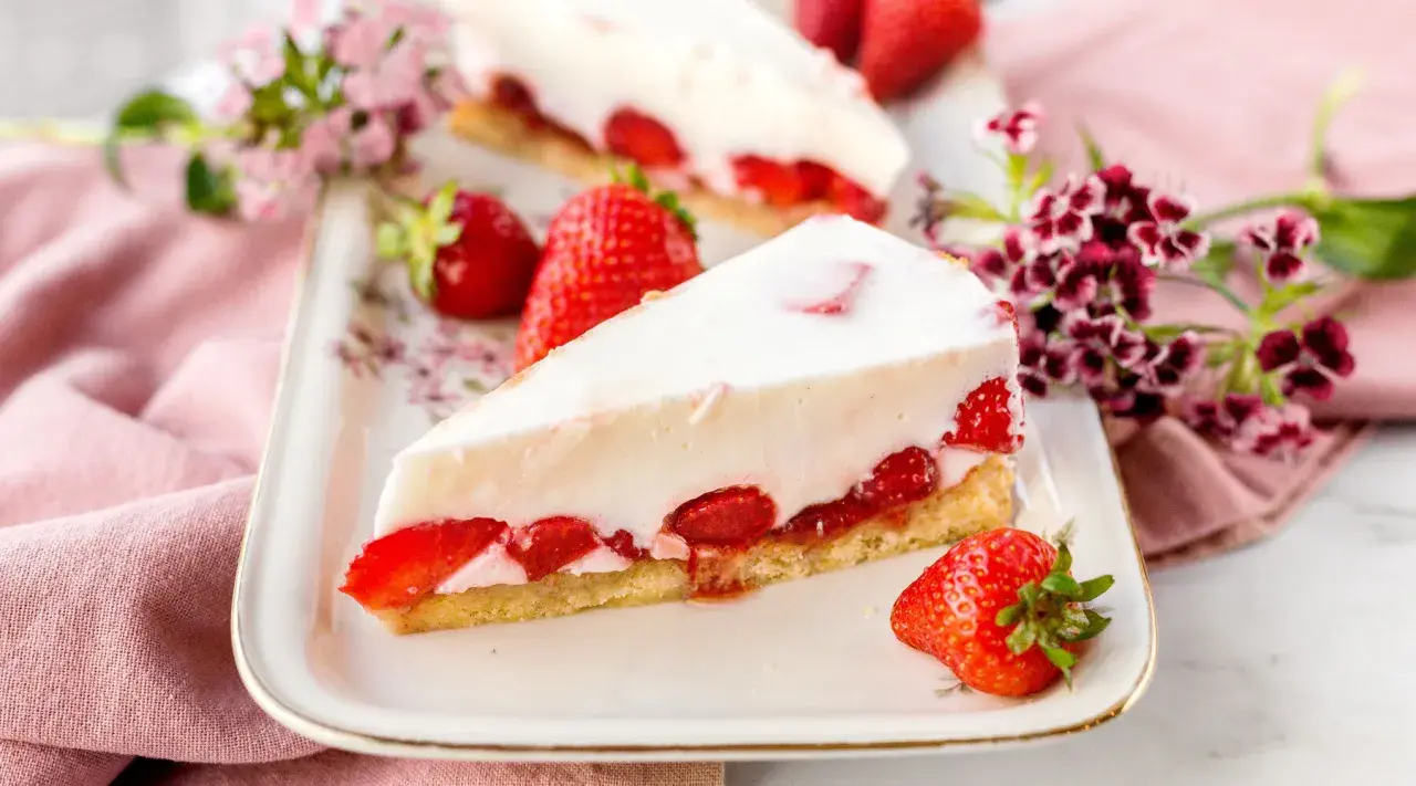 Ein Stück Erdbeerkuchen mit weißer Creme und frischen Erdbeeren auf einem Teller.